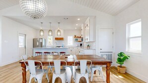 A spacious kitchen with white cabinets, a wooden dining table, and pendant lights. - Pet Friendly Beach Home, Shared Pool, Boardwalk to the Beach, Golf Cart Included (Port Aransas)