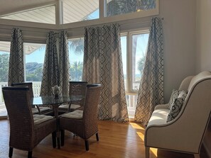 A dining area with a glass table and wicker chairs, a white sofa, and patterned curtains. - Inlet Sunset - 2nd Row and Creekfront! (Garden City)