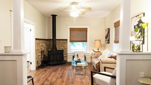 A living room with a stone fireplace, a ceiling fan, and a window with blinds. - Anderson Cottage: comfy 3 bedroom near stadium, winery, airport, & golf course! (Manhattan)
