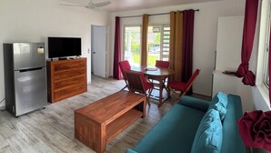 A modern living room with a teal sofa, wooden coffee table, and a dining area with red chairs. - Painapo - Mirimiri Lodge (Tumaraa)
