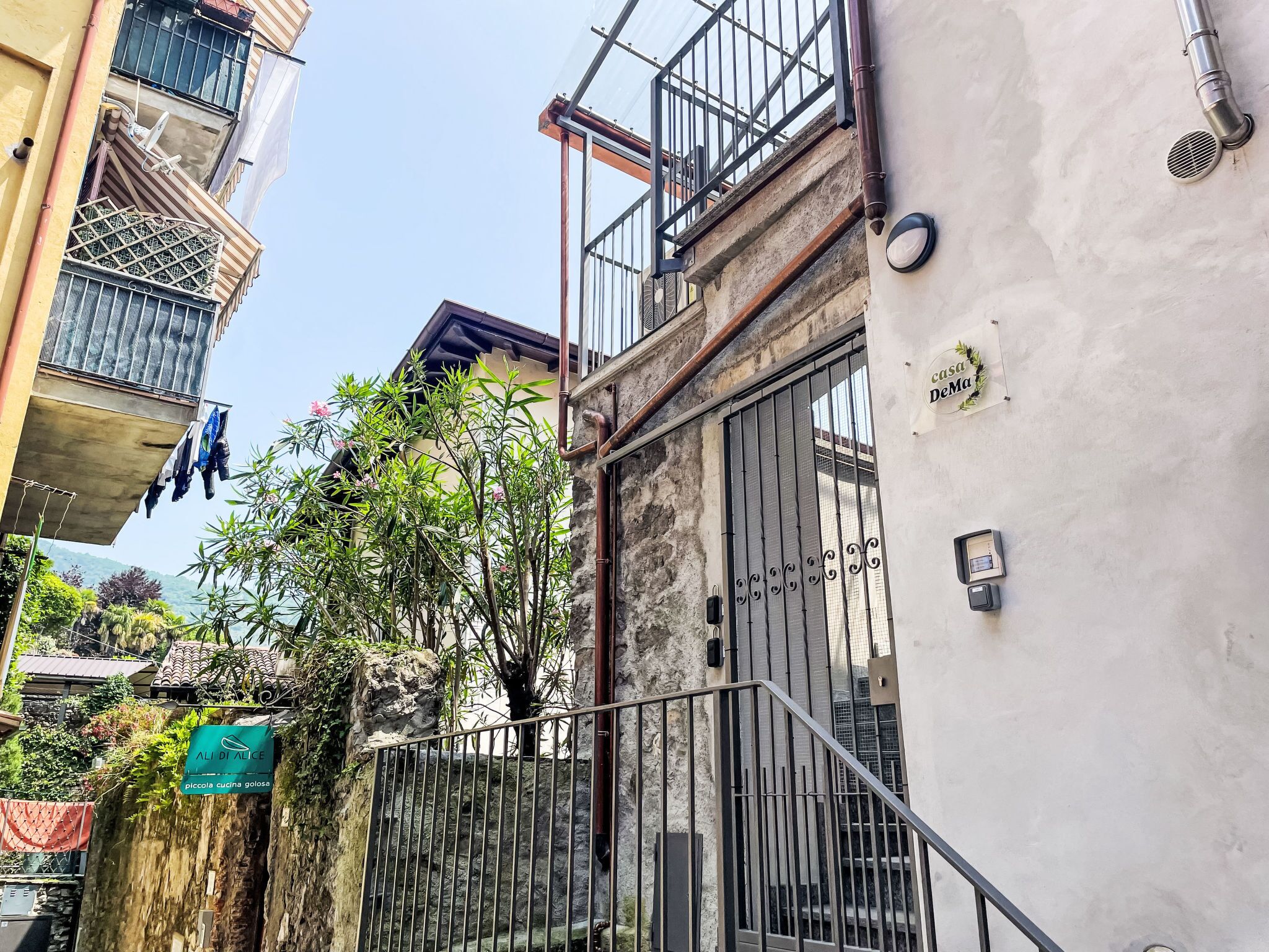 A narrow alley with a gated entrance, a sign for 'ALI DI ALICE', and a building with a balcony.
