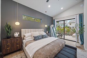 Een moderne slaapkamer met een groot bed, nachtkastjes, een kamerplant en uitzicht op het buiten.
