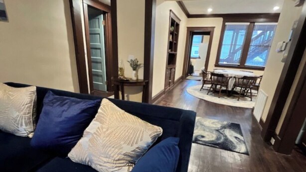 Una sala de estar con un sofá azul oscuro, un comedor con una mesa y sillas, y un pasillo que conduce a otra habitación.