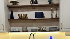 Una cocina con armarios blancos, encimera negra y pileta de acero inoxidable. Hay estantes sobre la pileta con diversos utensilios de cocina.