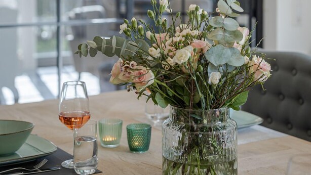 A dining table set with a vase of flowers, a wine glass, and a candle. - Baileys Hüs - Lovingly renovated "Baileys Hüs" in the picturesque village of Keitum on (Keitum)