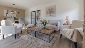 A modern living room with a sofa, armchairs, a coffee table, and a dining area with a chandelier. - Baileys Hüs - Lovingly renovated "Baileys Hüs" in the picturesque village of Keitum on (Keitum)