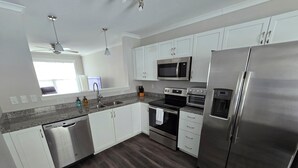 Una cocina moderna con armarios blancos, electrodomésticos de acero inoxidable, lavavajillas y piso de madera.