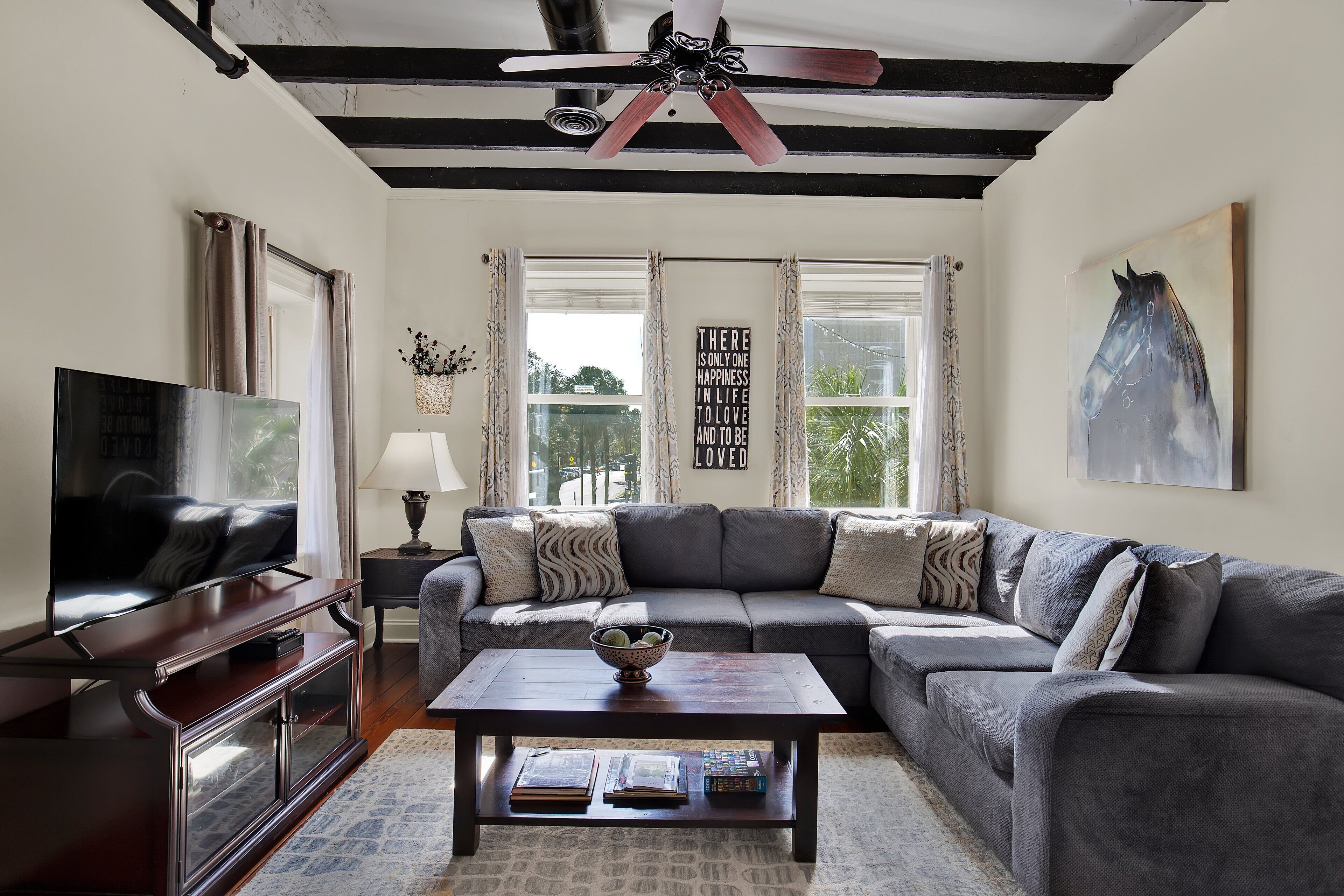 A living room with a large sectional sofa, a coffee table with books, a television on a stand, and a ceiling fan.