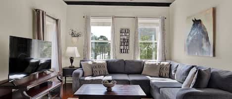 A living room with a large sectional sofa, a coffee table with books, a television on a stand, and a ceiling fan.