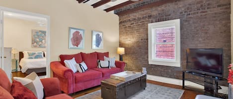 A living room with a red sofa, a wooden coffee table, and a television. There is a brick wall and a ceiling fan.