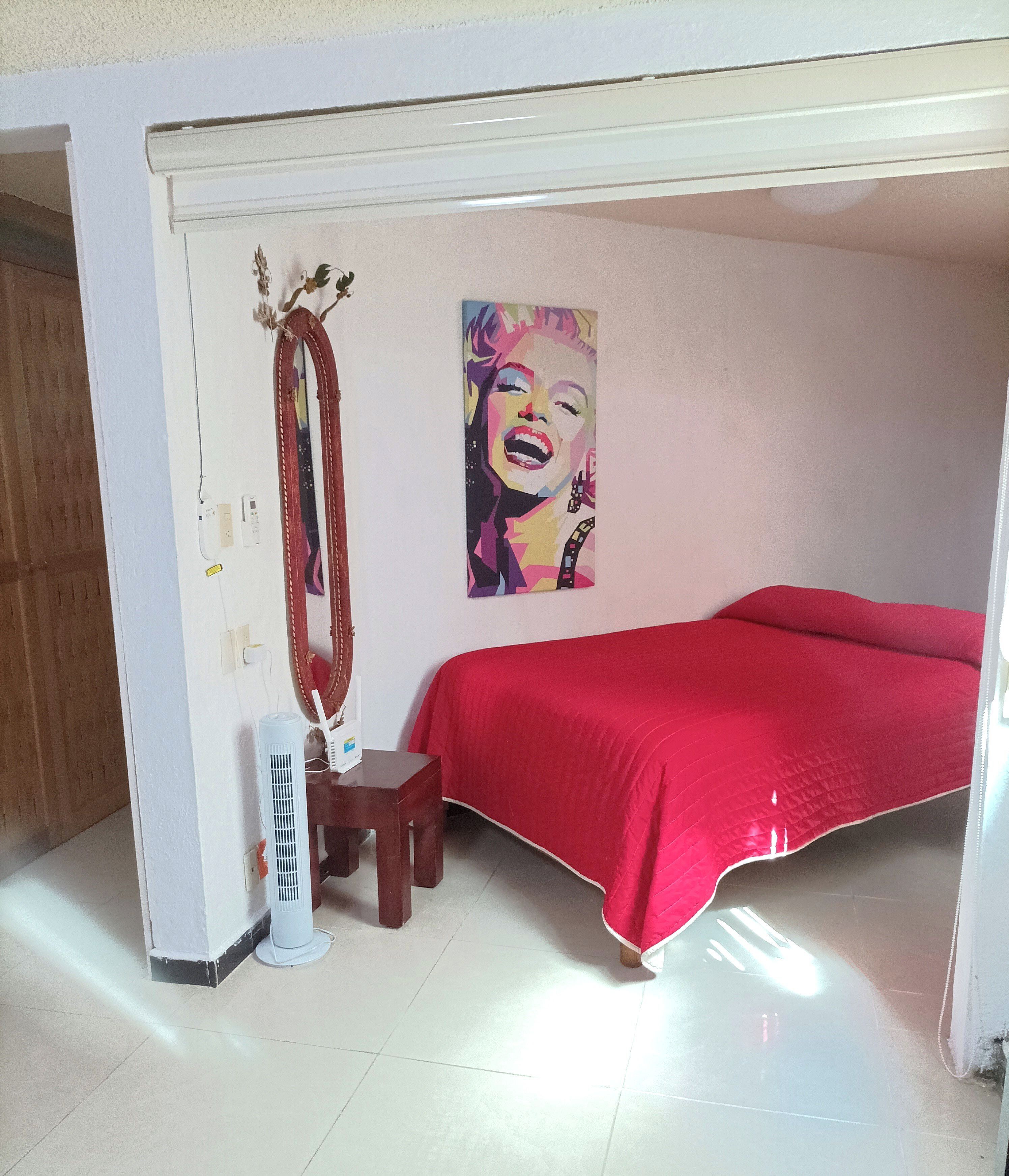 A bedroom with a red bedspread, a large mirror, and a poster on the wall.