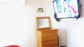 Une chambre à coucher comprenant un lit, une commode en bois, une petite table, un téléviseur fixé au mur et un radiateur.