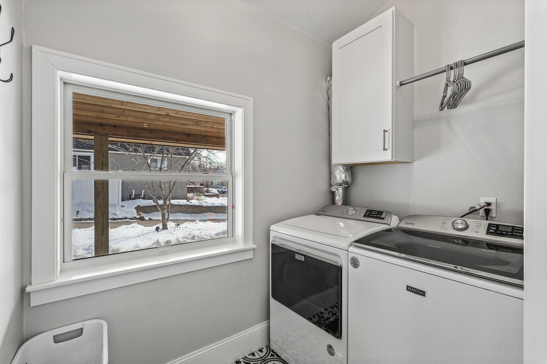 A compact laundry room with a washing machine, dryer, and a window with a view of a snowy landscape.