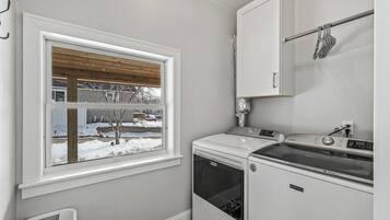 A compact laundry room with a washing machine, dryer, and a window with a view of a snowy landscape.