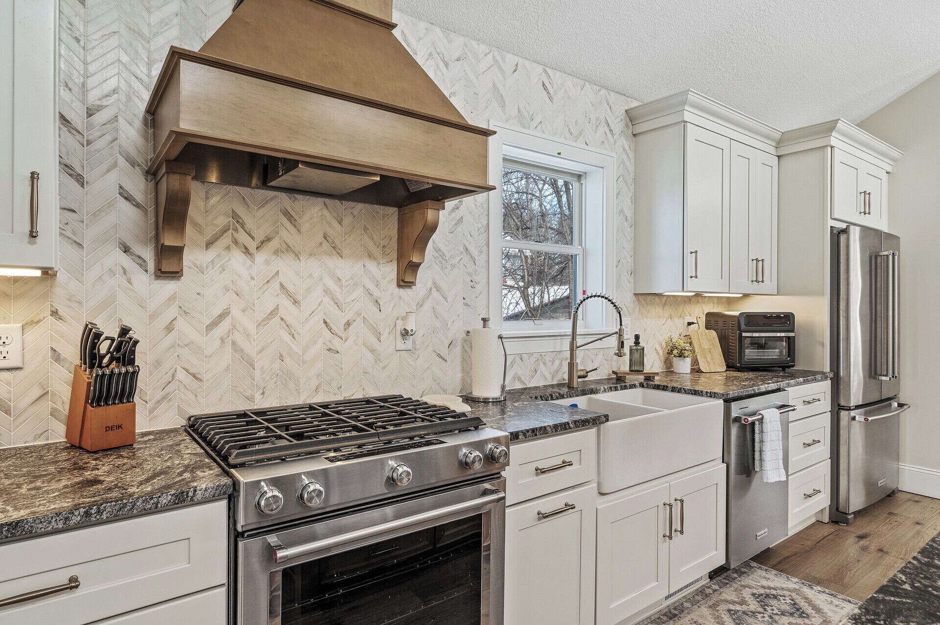 Una cocina moderna con armarios blancos, una estufa de acero inoxidable, un horno empotrado y un refrigerador.