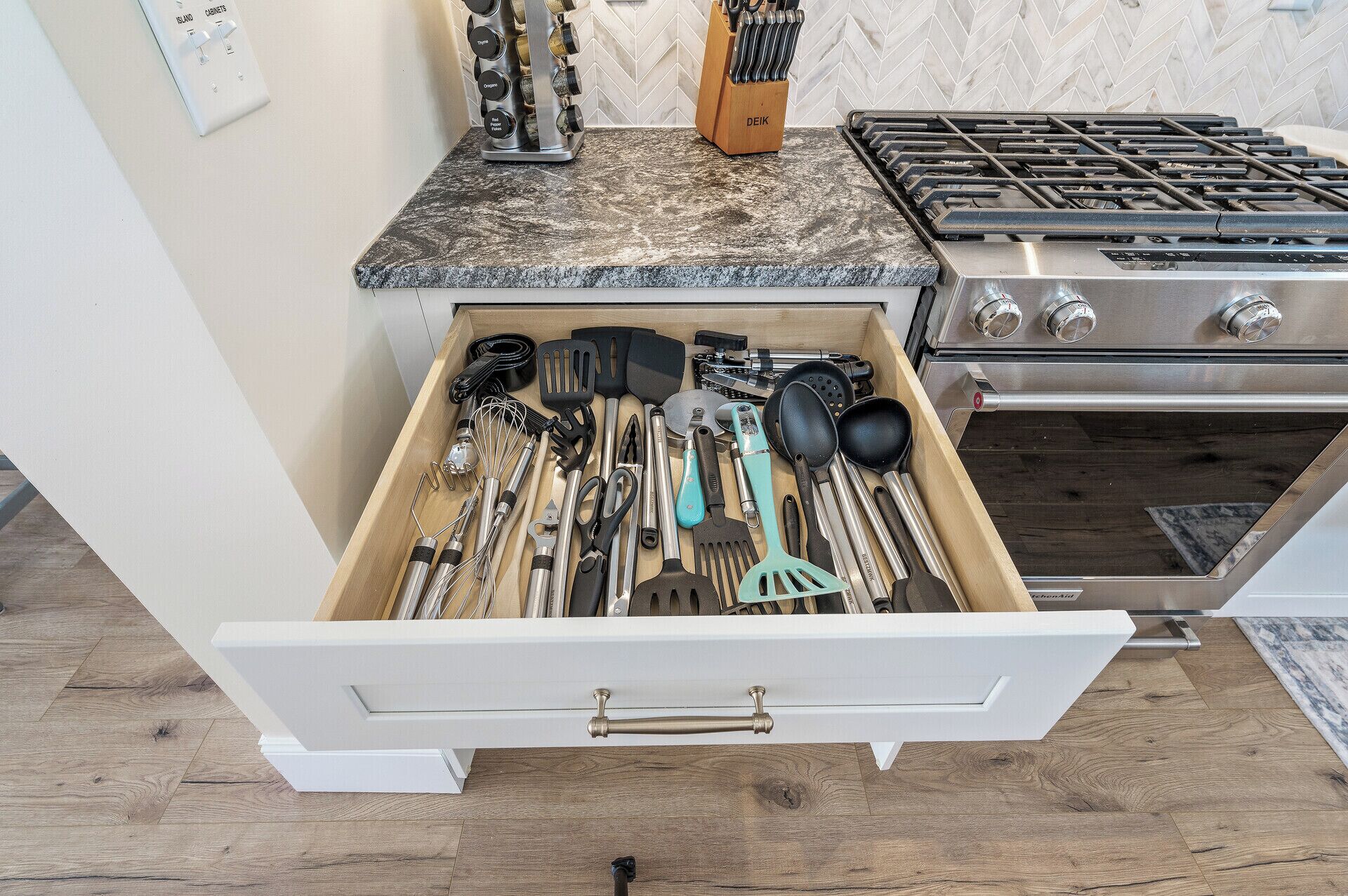 A kitchen with a drawer containing various utensils and a stove.