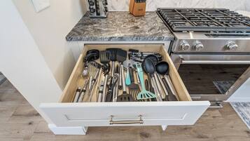 A kitchen with a drawer containing various utensils and a stove.