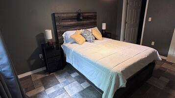 Een slaapkamer met een bed, nachtkastje, lamp, plafondventilator en een deur.