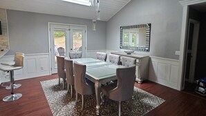 Et spiseområde med et bord med glasplade, grå polstrede stole og et gulvtæppe med et mønster.
