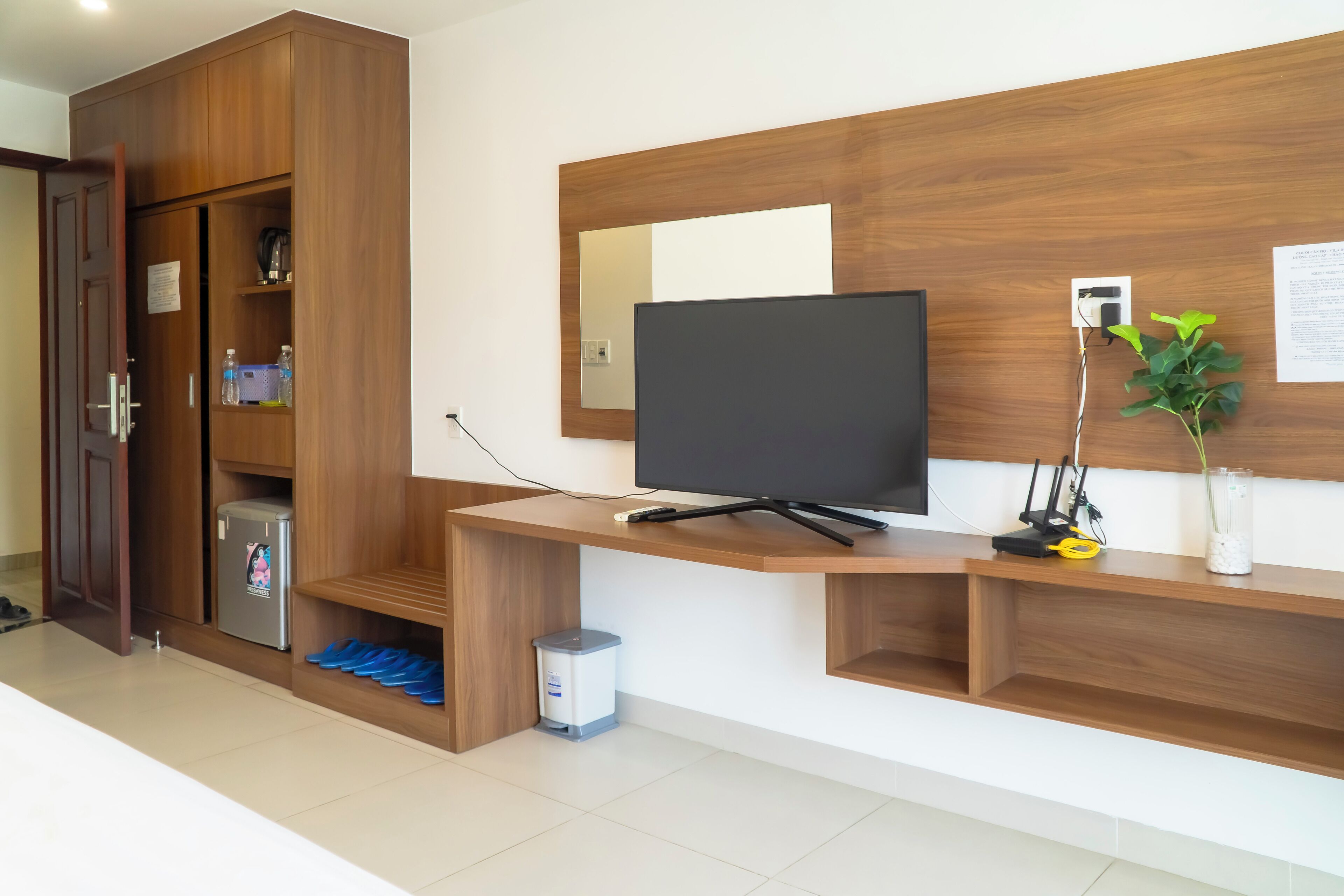 Una sala de estar moderna con un mueble de entretenimiento de madera, un televisor de pantalla plana y un refrigerador pequeño.