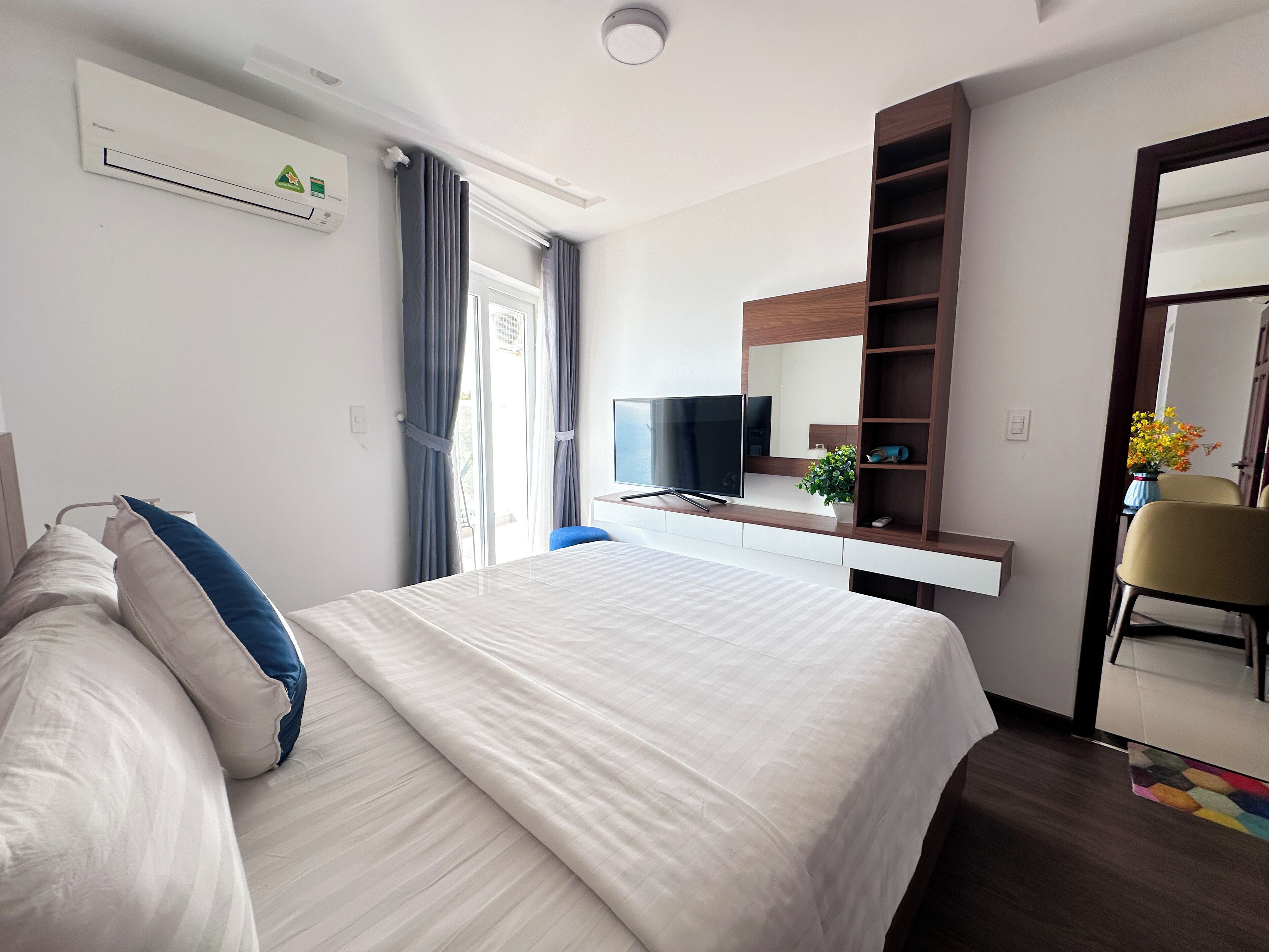 A modern hotel room with a large bed, a flat-screen TV, a desk with a computer, and a mirror.