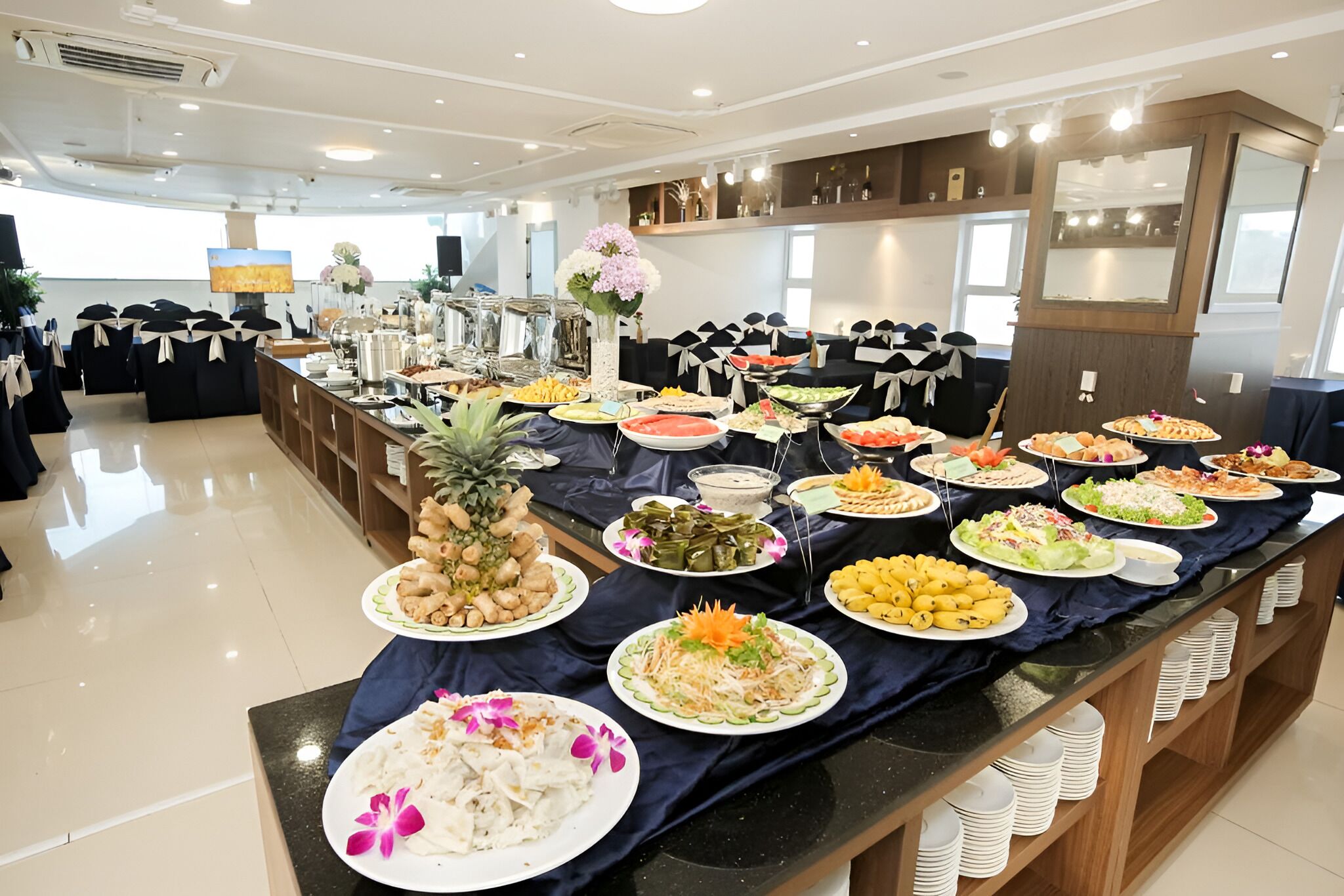 A buffet setup with various dishes and a large screen in the background.