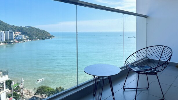 Un balcón con vista despejada al mar, una mesa redonda y dos sillas de metal ligero.