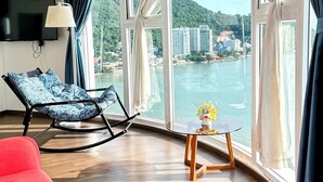 Una habitación moderna con un ventanal grande, un sofá rojo, un sillón azul estampado y una mesita con un jarrón.