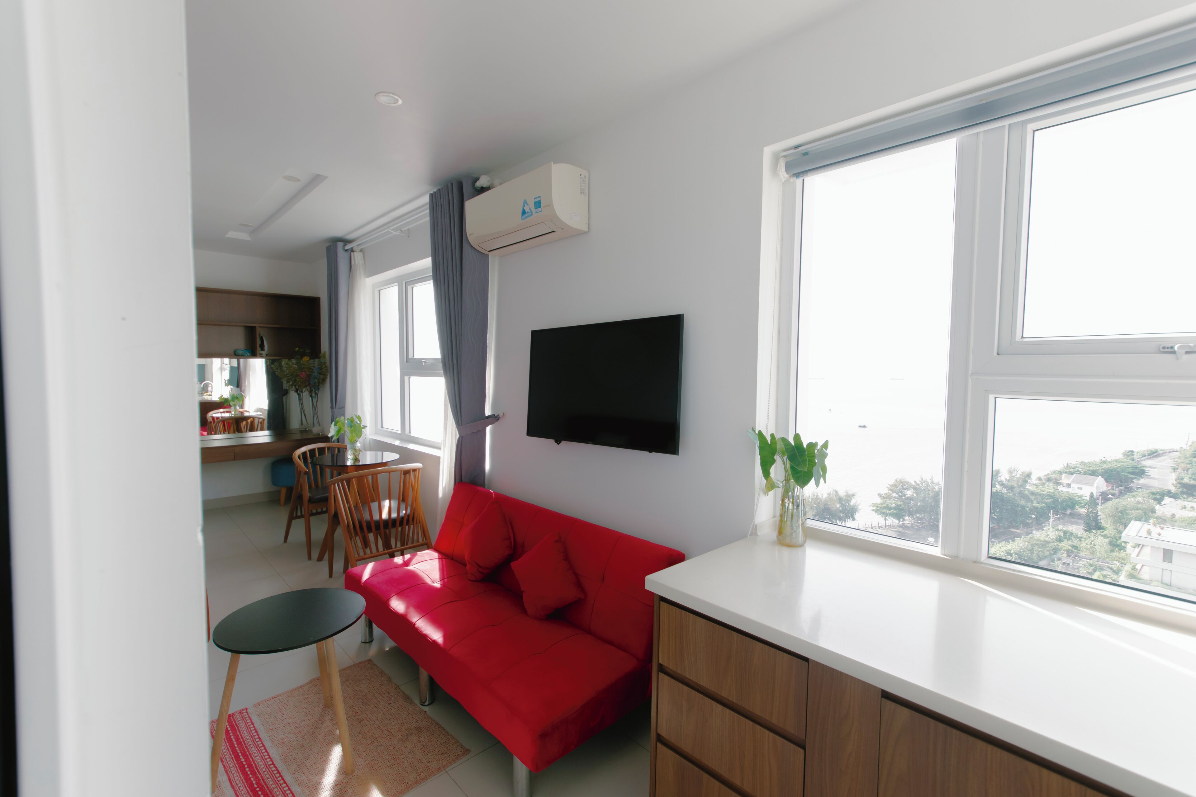 A compact living space with a red sofa, a small dining table, and a TV mounted on the wall.