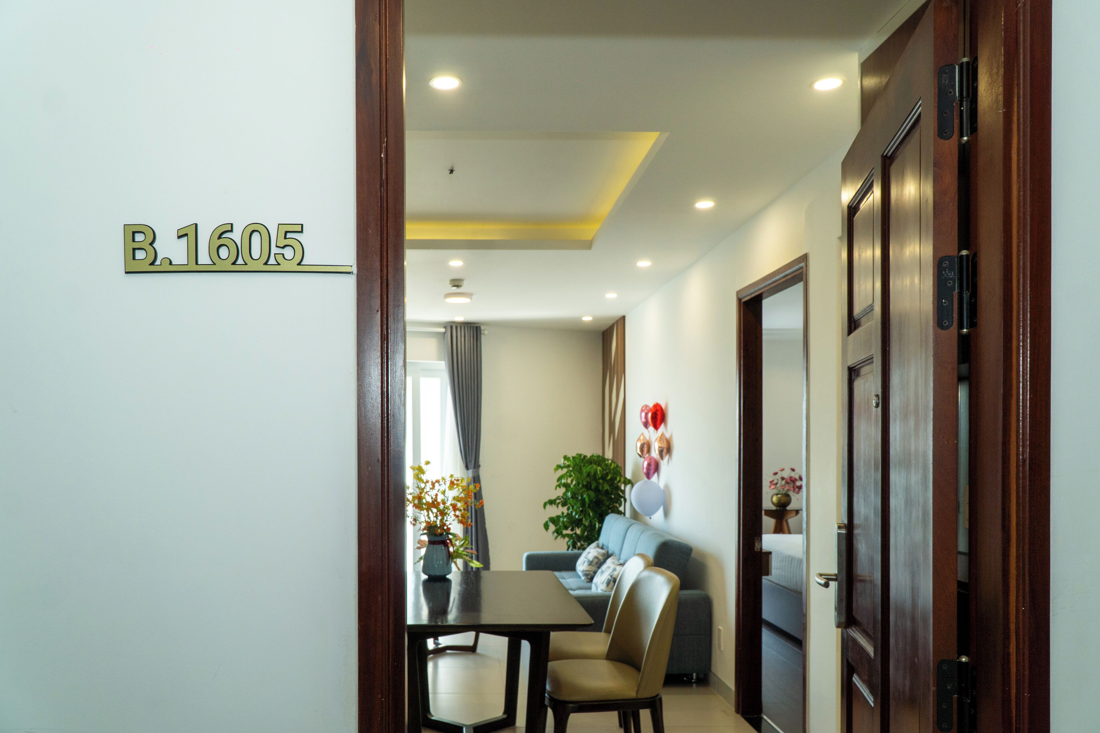 Une chambre d’hôtel comprenant un coin repas, un canapé, une plante en pot et une porte avec un numéro.