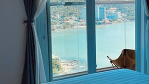 Una habitación con una cama, una silla y un amplio ventanal que ofrece vistas a un cuerpo de agua y edificios.