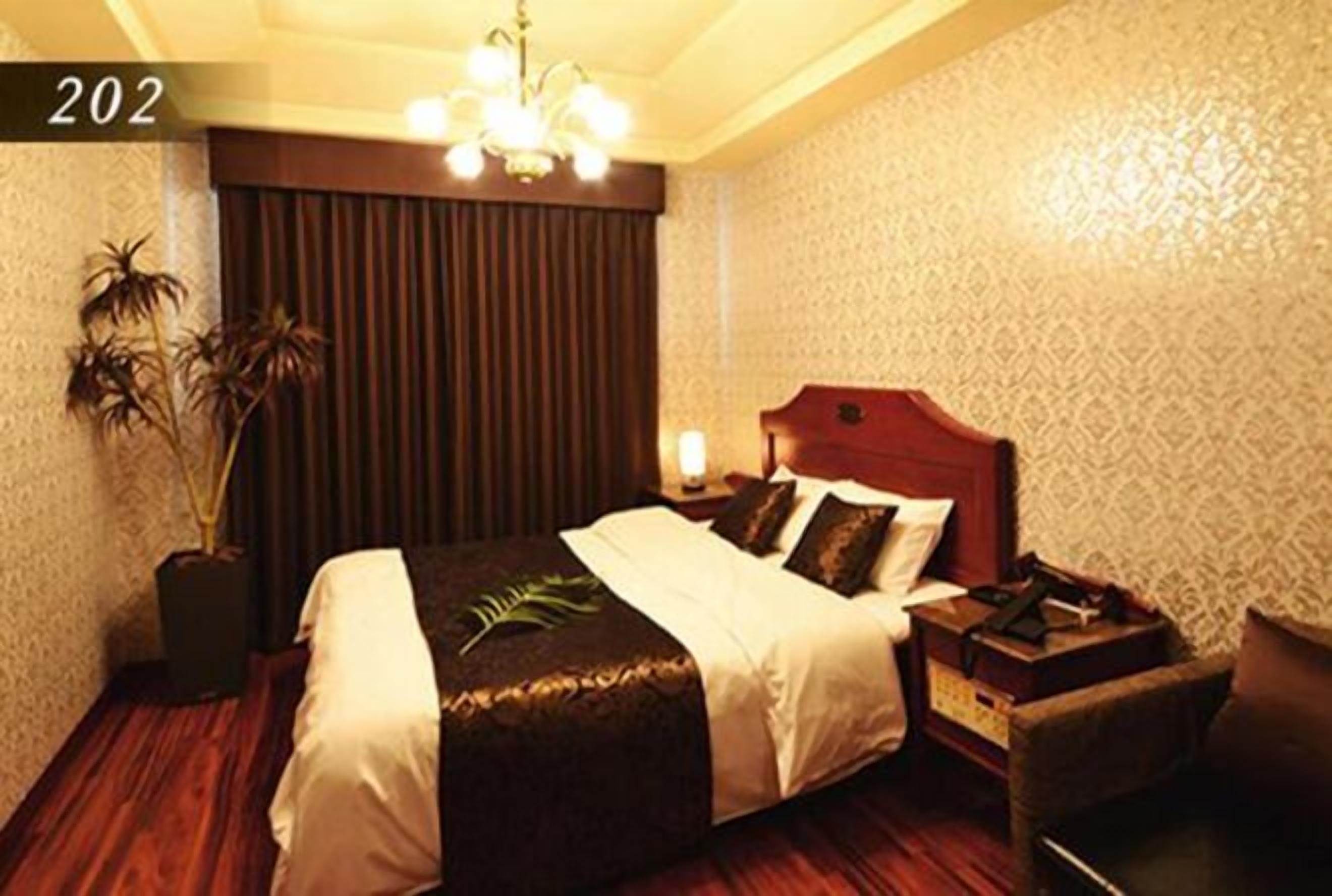 Quarto de hotel com uma cama grande, uma mesa de cabeceira, uma cadeira e uma planta em vaso.