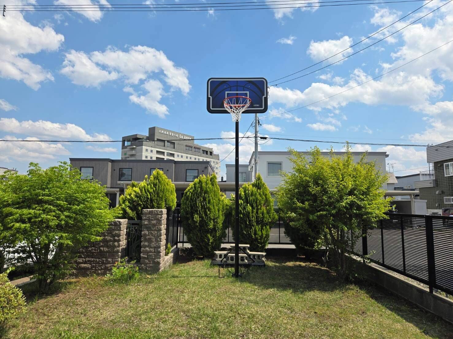 A basketball court with a net, surrounded by greenery and residential buildings.