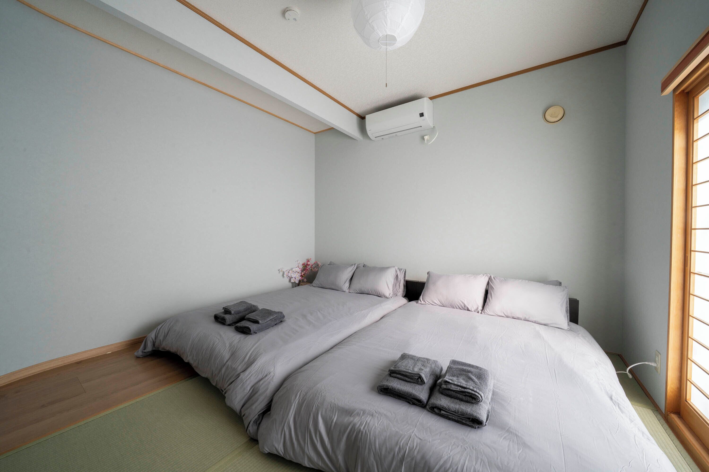 A bedroom with two beds, a ceiling fan, a window, and a wall-mounted air conditioner.