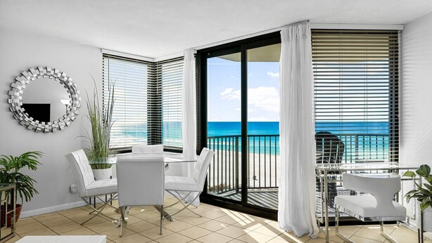A balcony with a view of the ocean, white furniture, and a round mirror on the wall.