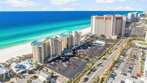 A coastal hotel with multiple buildings, a parking lot, and a beach view.