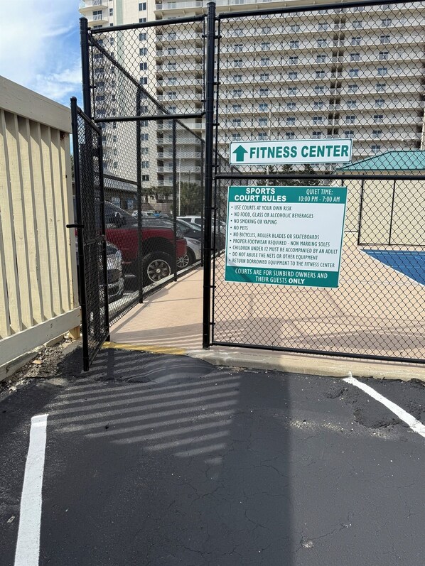 A gated entrance to a fitness center with a sign listing sports court rules and quiet time hours. - Beachfront 1BR Condo, Pools, Gym and Stunning Views! (Panama City Beach)