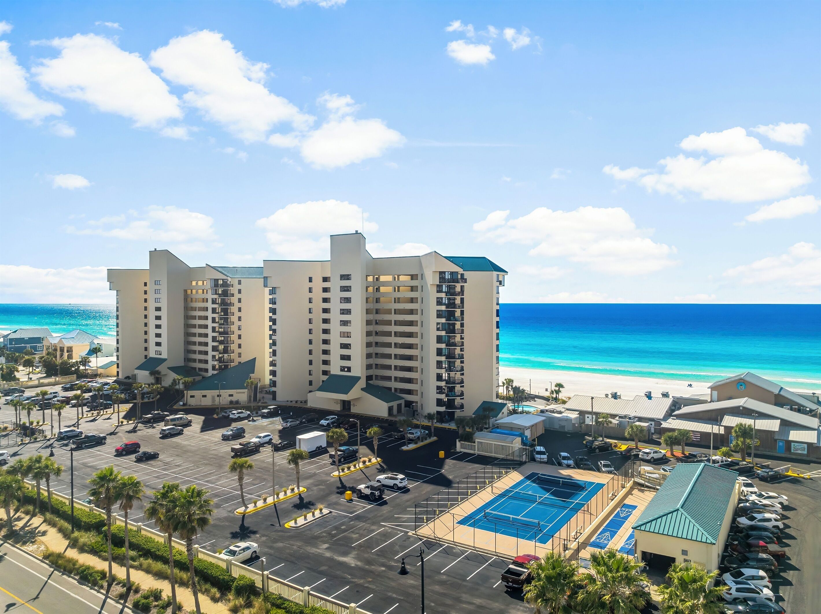 A hotel with multiple floors, a parking lot, and a beach view.