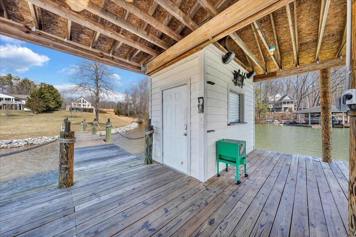 A wooden deck with a white building, a green bench, and a view of a lake.