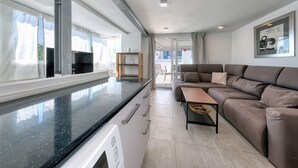 Een moderne keuken met een zwart aanrecht en witte kasten, een bruine leren bank en een houten bijzettafeltje.