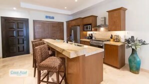 A modern kitchen with a central island, wooden cabinets, and a dining area with wicker chairs.