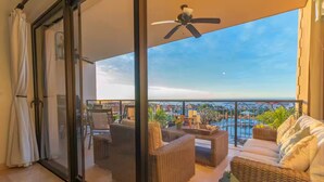A balcony with wicker furniture, a ceiling fan, and a view of a pool and cityscape.