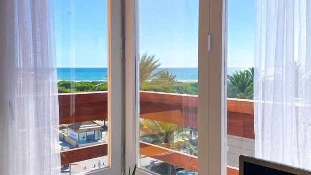 Una habitación con un gran ventanal que ofrece vistas al océano y un edificio distante.