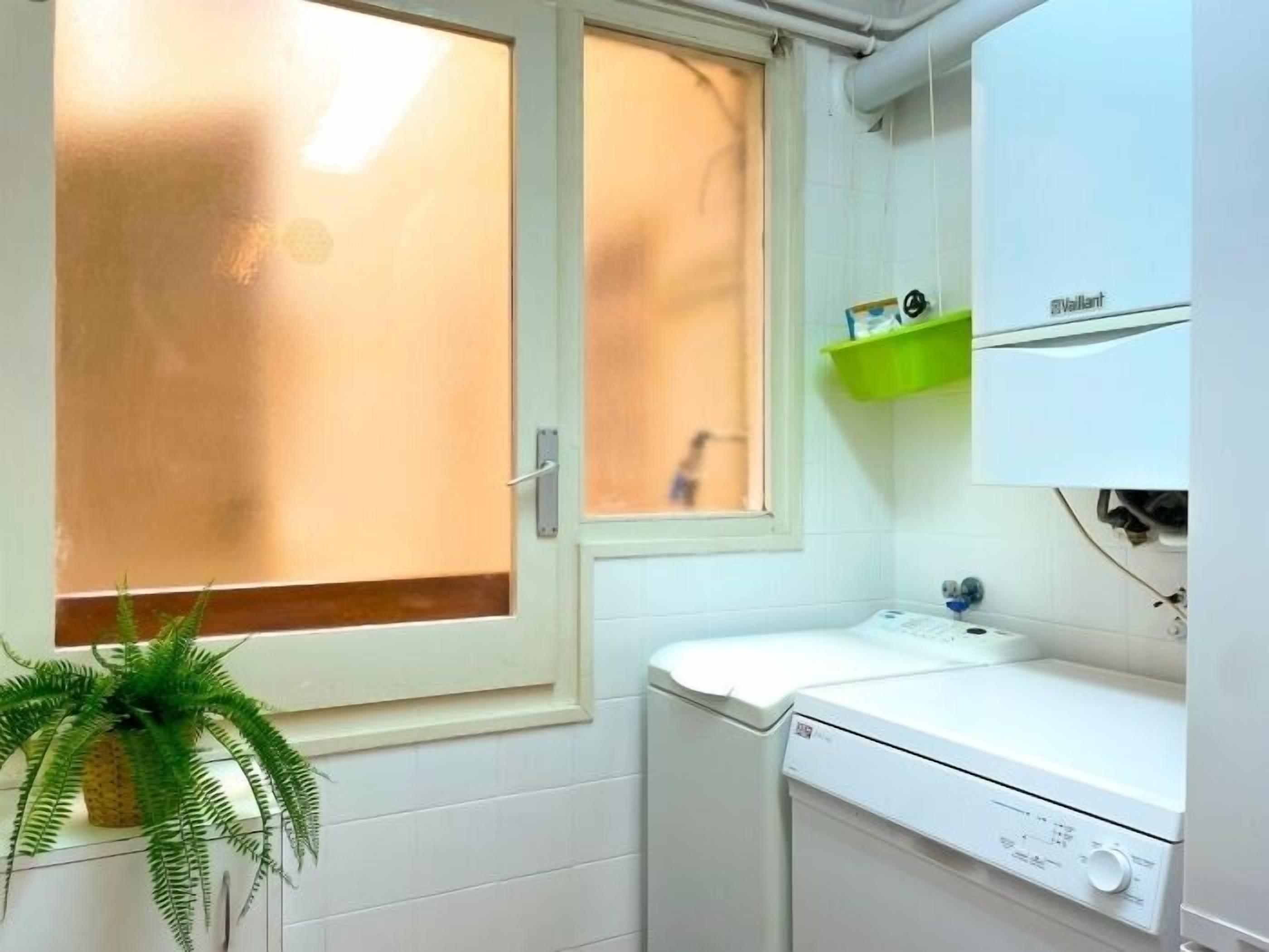 Pequeña y limpia sala de lavandería con lavadora, secadora y una ventana con vidrio esmerilado.