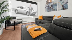 Un salon moderne avec un grand téléviseur à écran plat, un canapé en cuir noir, un plaid jaune et une télécommande posée sur le canapé.