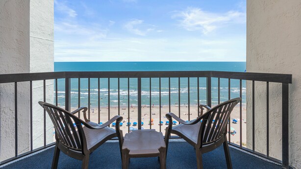 A balcony with two chairs facing a beach.