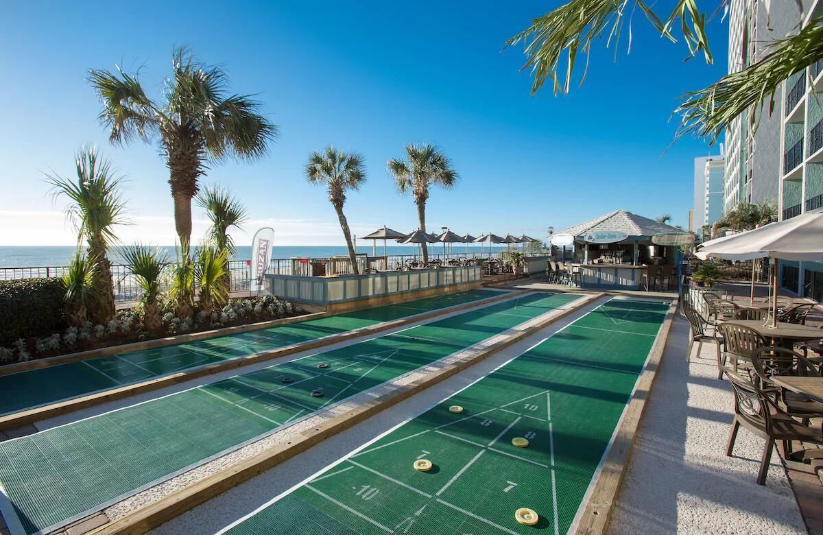 A pool table area with a view of the ocean, palm trees, and outdoor seating.