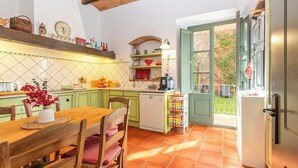 Uma cozinha com mesa de madeira, cadeiras, lava-louças e janela com vista para o verde.