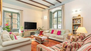 Uma sala de estar com sofá, mesa de centro, televisão e estante de livros.