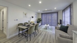 A modern living room with a sofa, a dining table with chairs, and a large window with blinds.